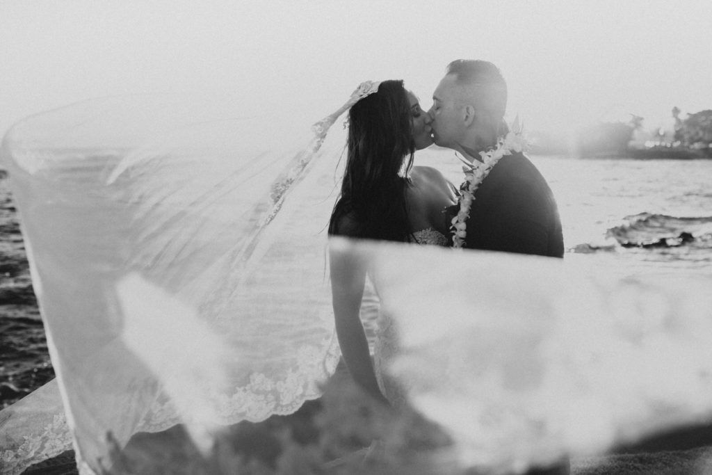 bride and groom kissing at sunset and veil blowing in the wind